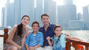 Joyful family capturing memories on a cruise in Singapore, posing against the scenic river backdrop, creating cherished moments together.